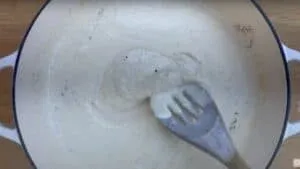Creamy white sauce being stirred in a pot with a wooden spoon.